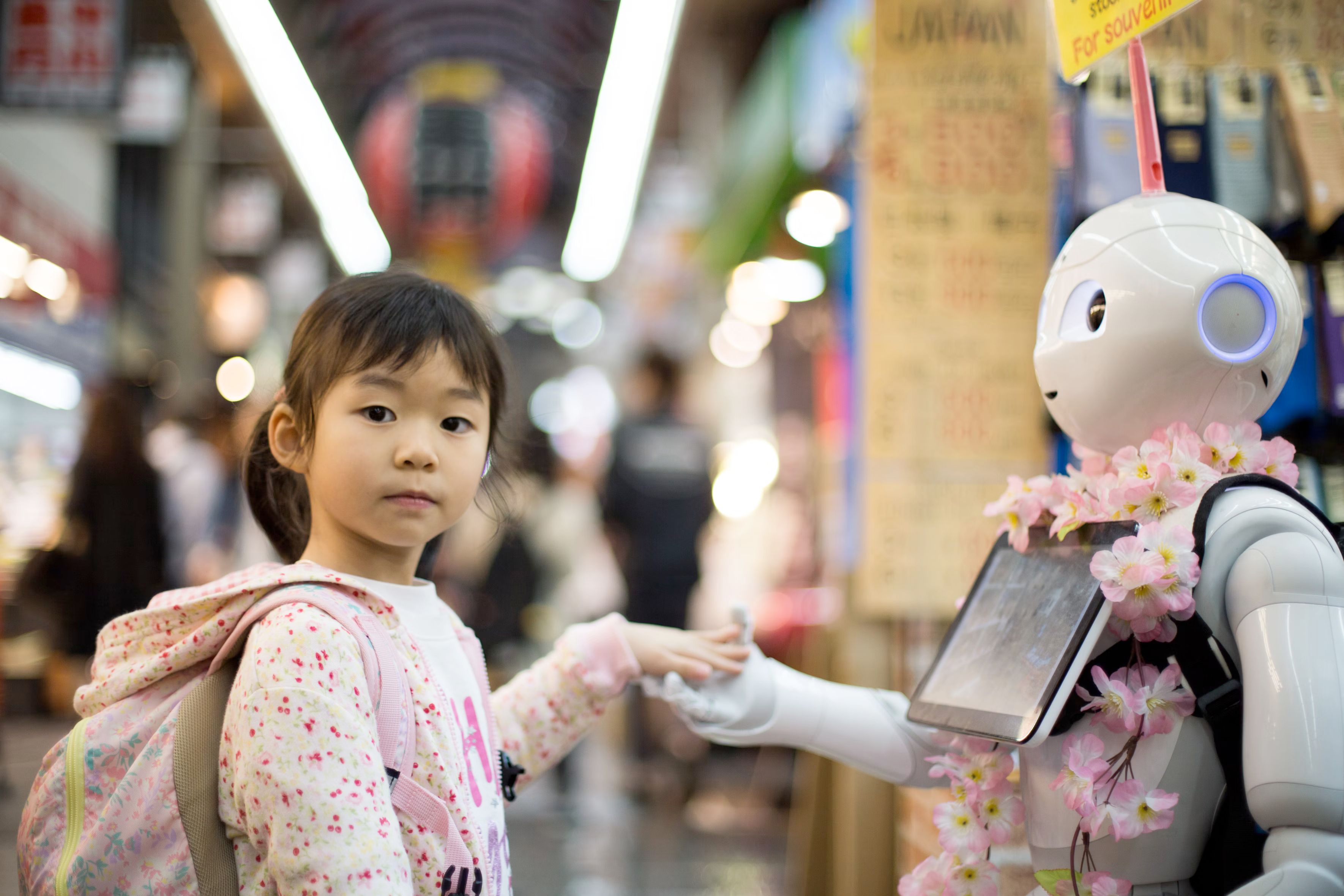 a little girl holding hands with a Pepper robot