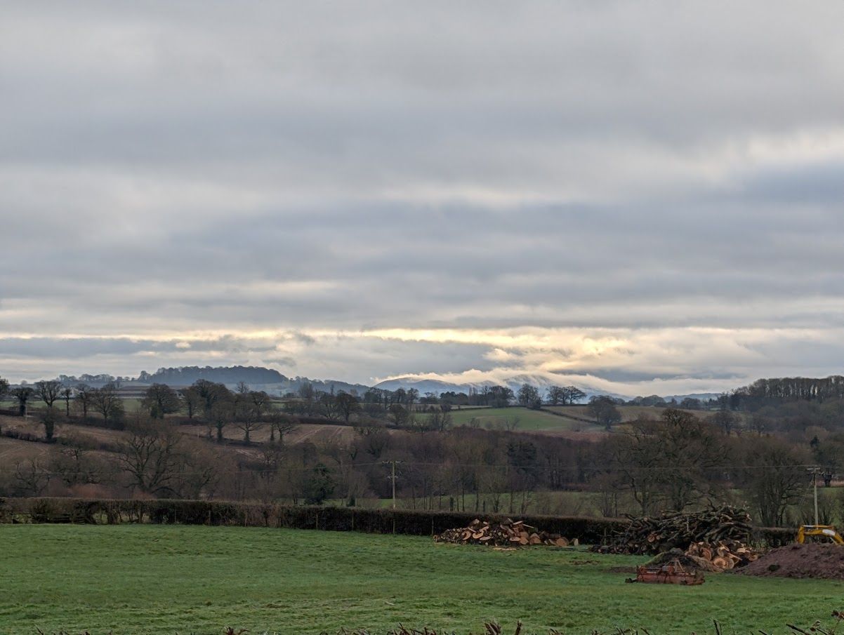 a photo of a field with mist gently settling over the top of the malvern hills in the background