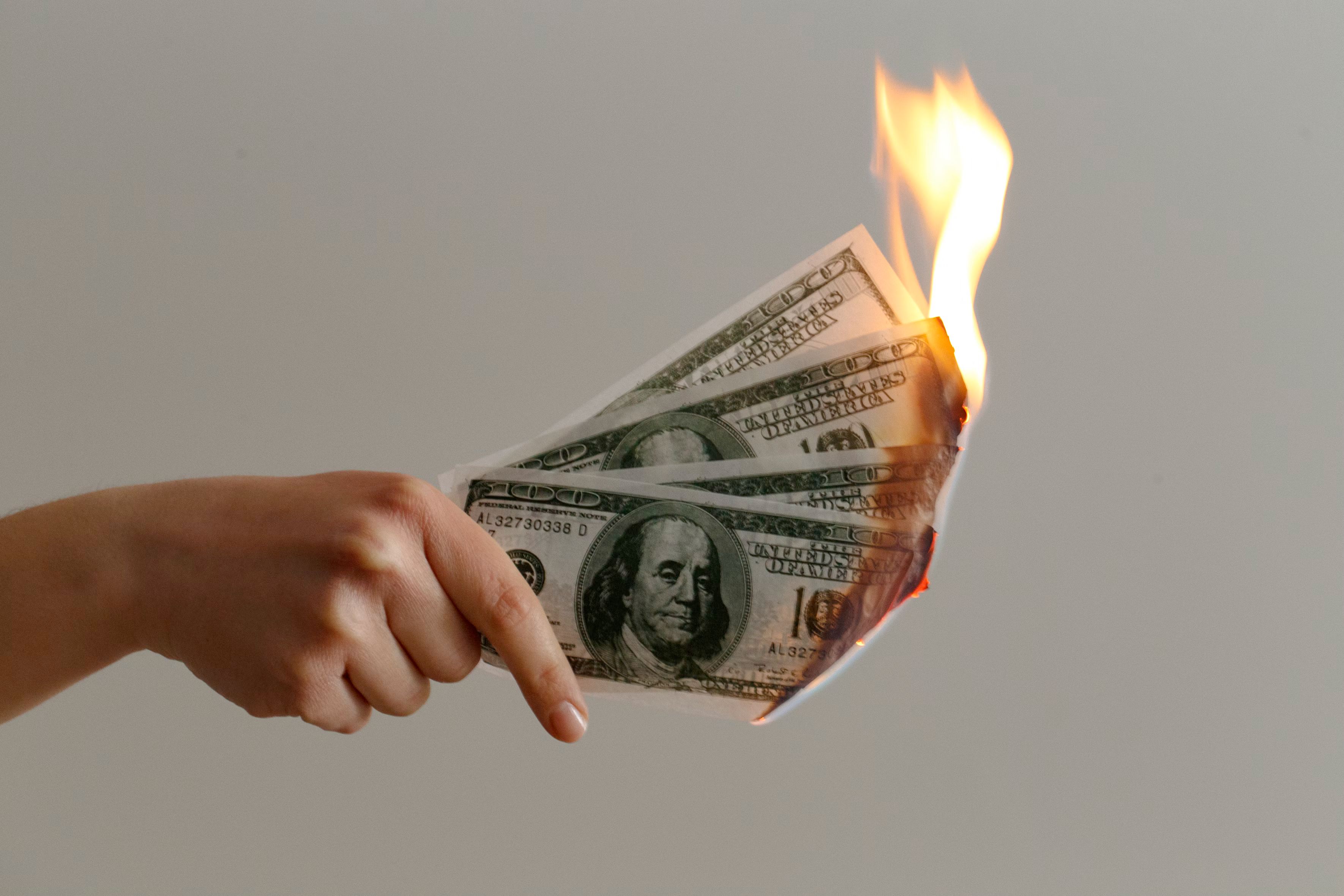 image of a hand holding some flaming 10 dollar notes.